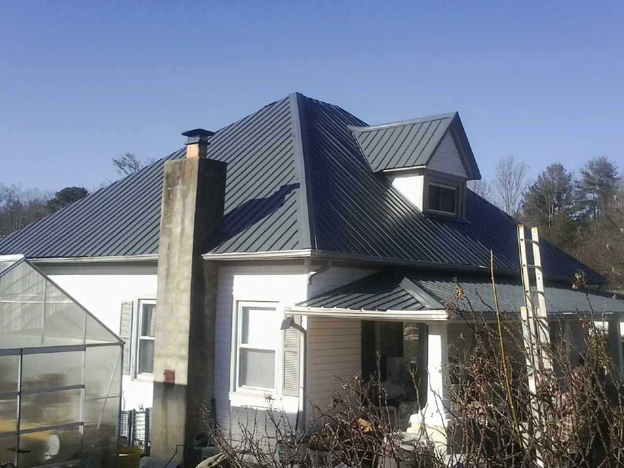 Dark blue standing seam metal roof on a white farmhouse with dormer — Slate & Tile Roof Repair by Roofing Brothers in Haynesville