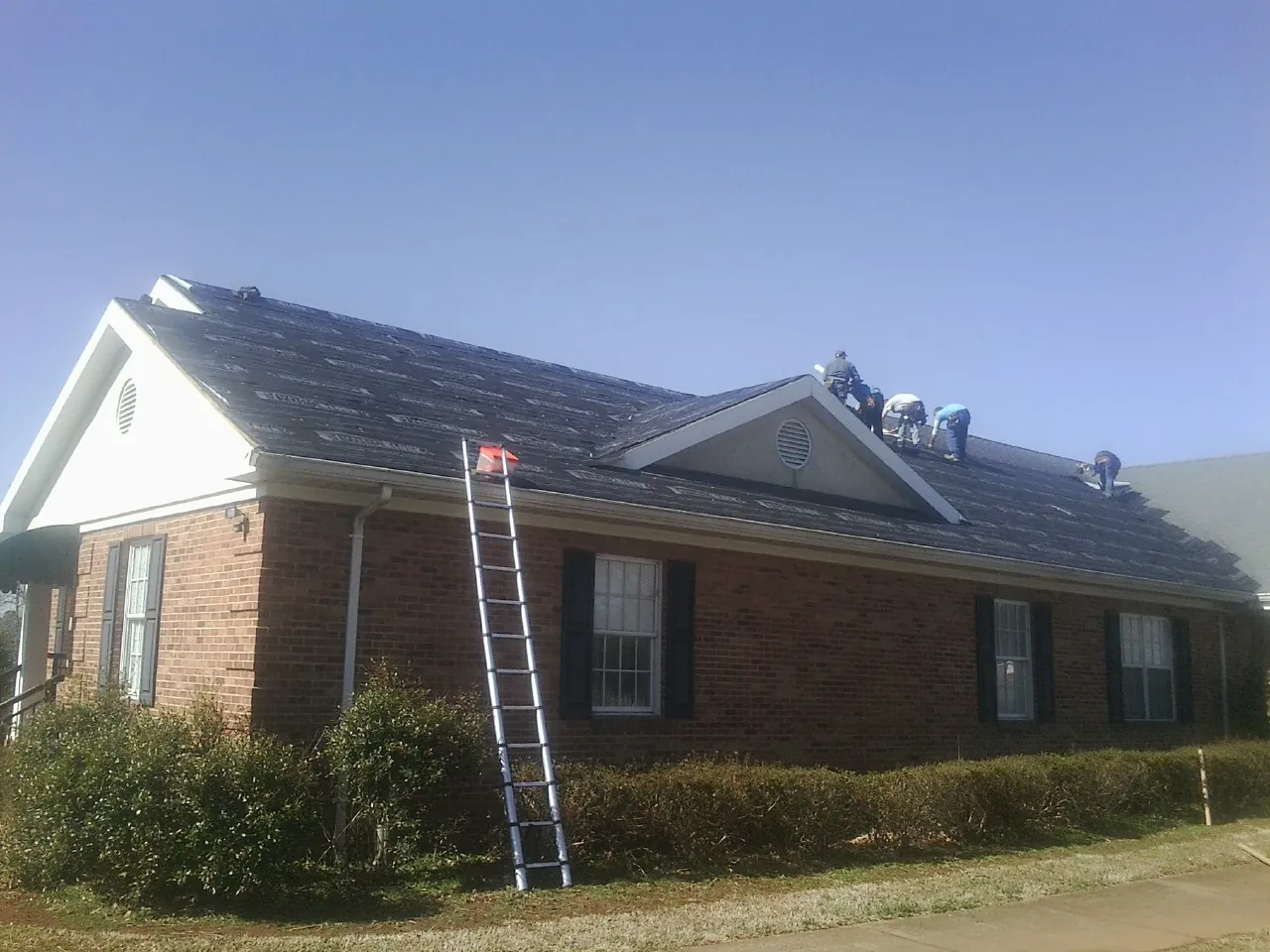 Crew tearing shingles off a brick ranch roof with a ladder set — Metal Roof Repair work by our crew in Haynesville