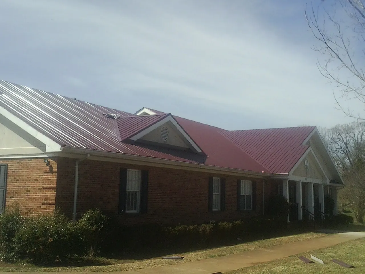 Red metal roof with gabled entries on a long brick building, from a Hail Damage Roof Repair job in Haynesville