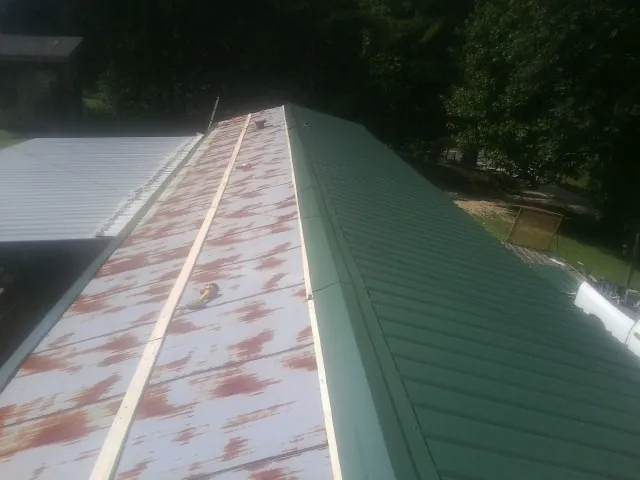 Old rusted panels beside newly installed green metal roofing — Wind Damage Roof Repair by Roofing Brothers in Haynesville