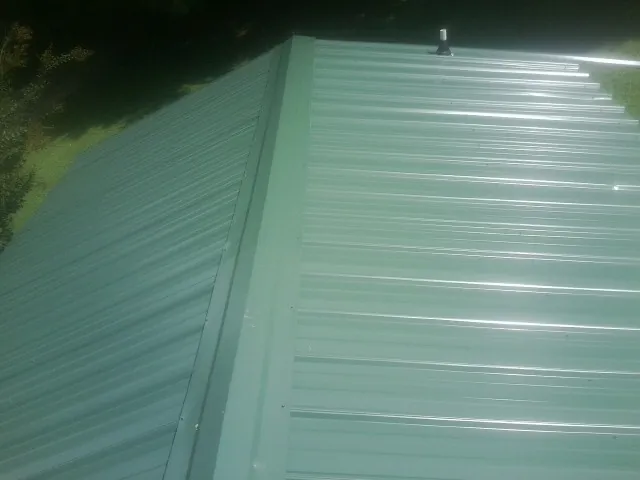 New green metal panels meeting at the ridge of a roof — Flat Roof Repair work by our crew in Haynesville
