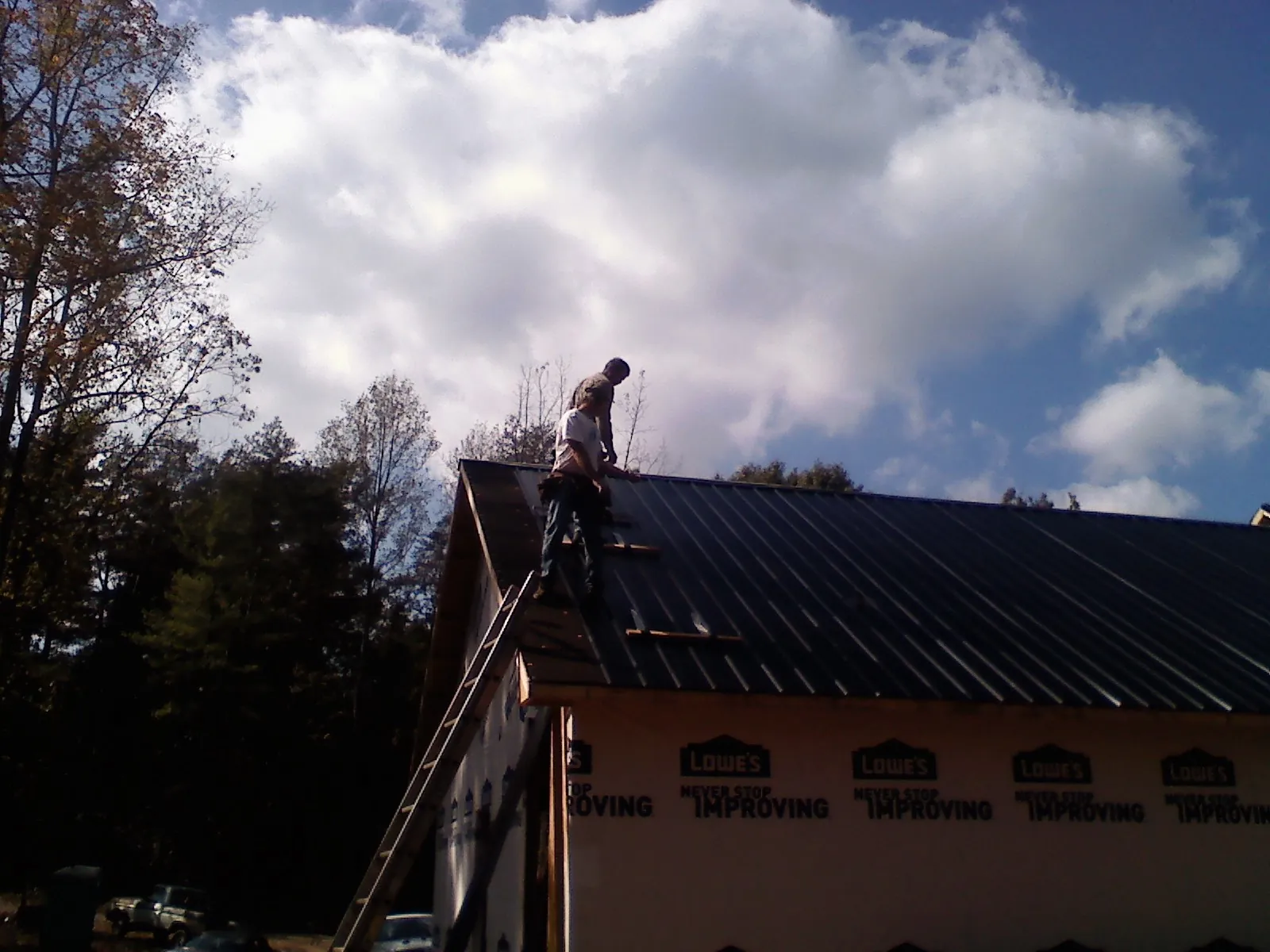 Roofer fastening dark metal panels high against a cloudy sky, from a Roof Inspection job in Haynesville