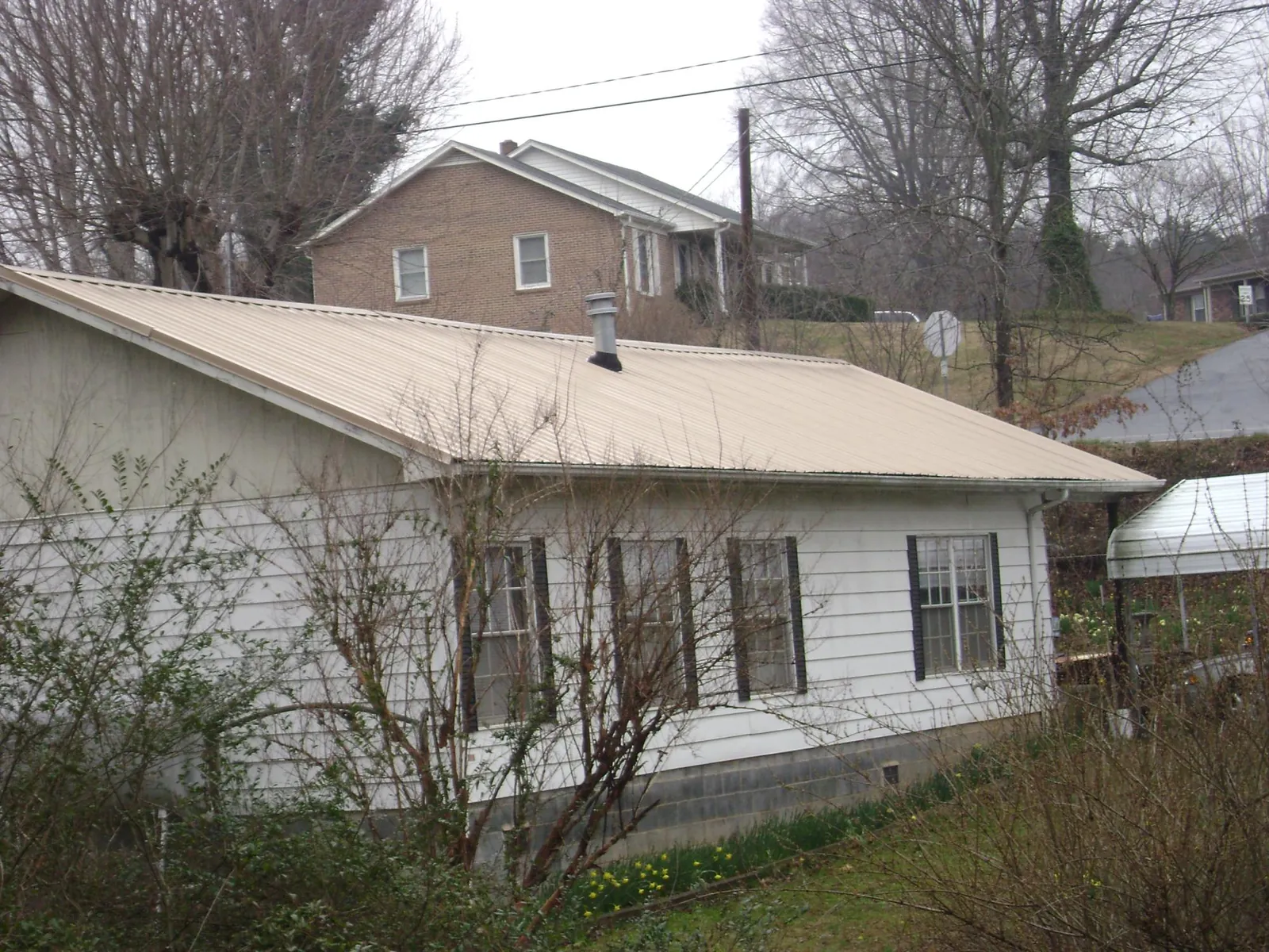 Tan metal roof on a white sided house set into a hillside — Commercial Roofing by Roofing Brothers in Haynesville