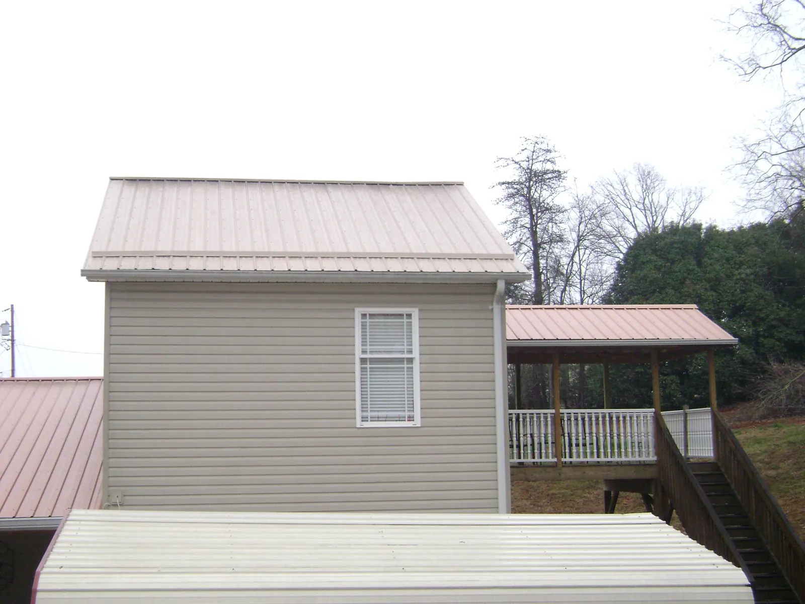 Tan metal roofs on a two story addition and attached porch, from a Roof Replacement job in Haynesville